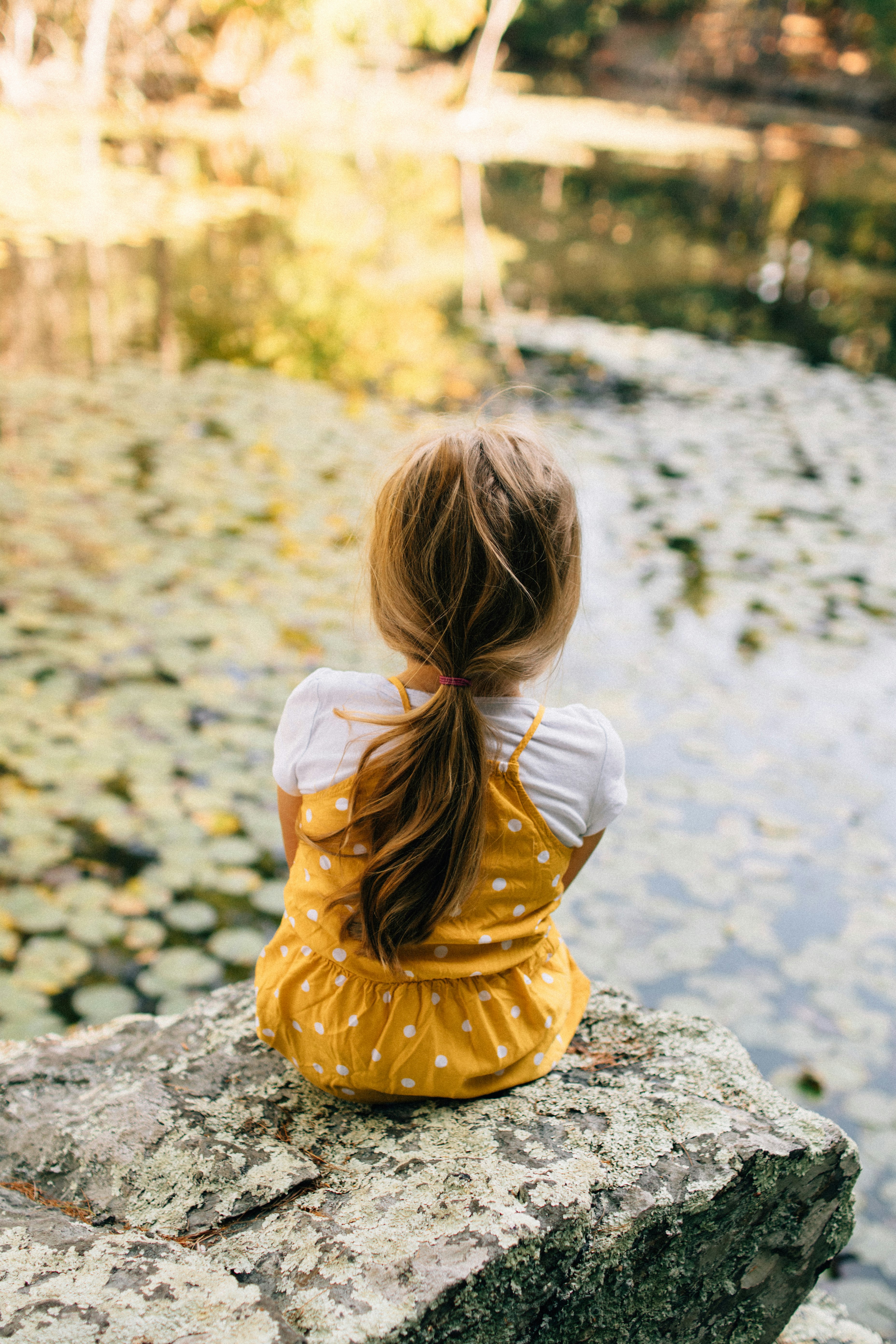 girl in yellow dress sitting on rock during daytime